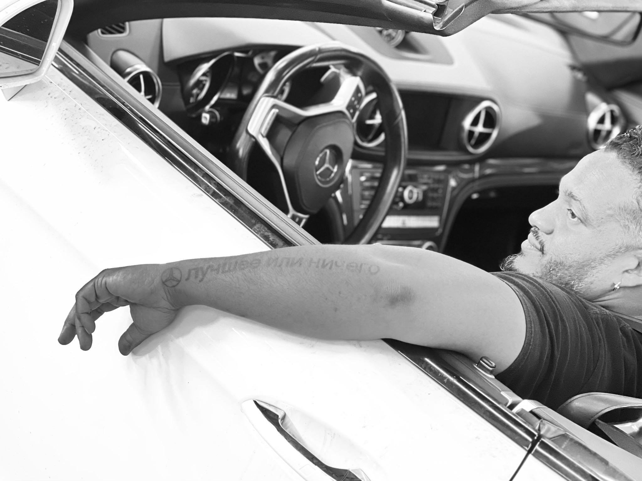 Black and white photo of a Federation Yard client's arm resting on a Mercedes-Benz door, tattooed with a Mercedes star and the words 'best or nothing'
